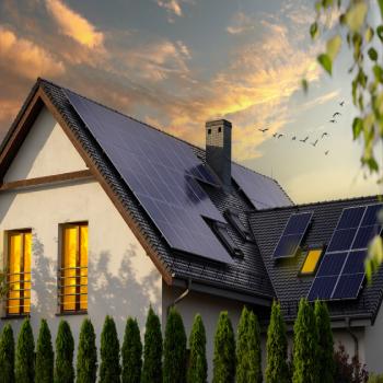 Kaksi henkilöä asentaa aurinkopaneeleita talon katolle